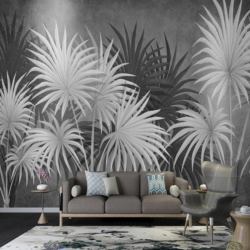 Papier peint panoramique Palmes noir et blanc : grandes palmes en éventail blanches et gris anthracite sur fond gris patiné, posé derrière un canapé