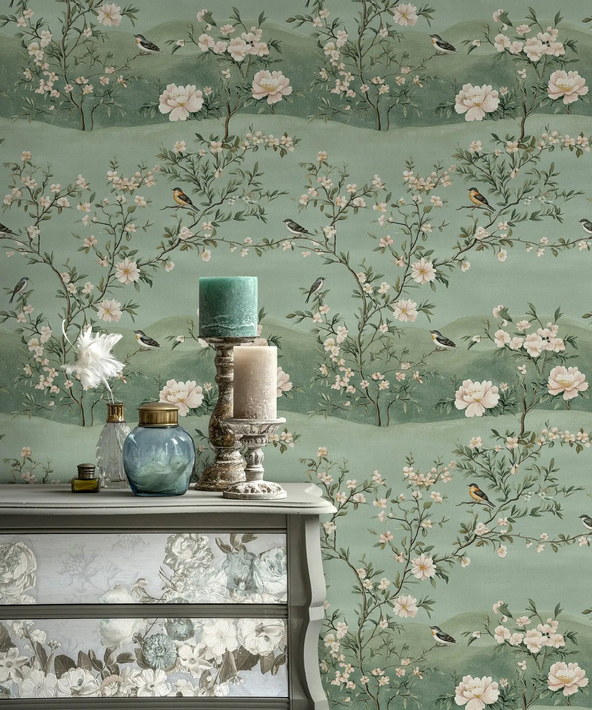 Papier peint panoramique Chinoiserie pivoines et collines vert d'eau : chinoiserie aux pivoines, arbustes fleuris et oiseaux sur des collines vert d'eau, au-dessus d'une commode patinée