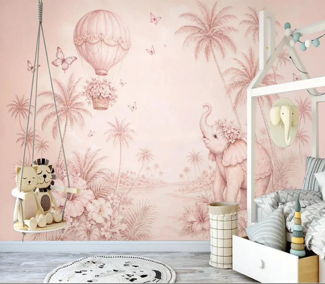 Papier peint panoramique Éléphant et montgolfière rose poudré : éléphanteau fleuri, montgolfière et palmiers en camaïeu rose poudré, posé dans une chambre d'enfant