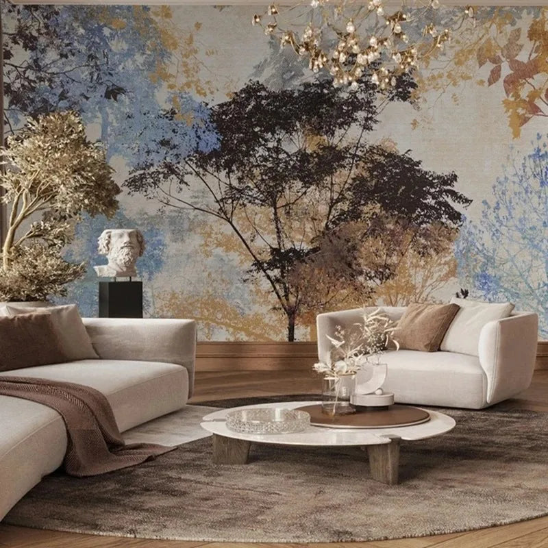Papier peint panoramique Arbres peints bleu et ocre : grand arbre brun entouré de feuillages bleus, ocre et gris, peint sur un fond lin patiné, posé derrière deux canapés