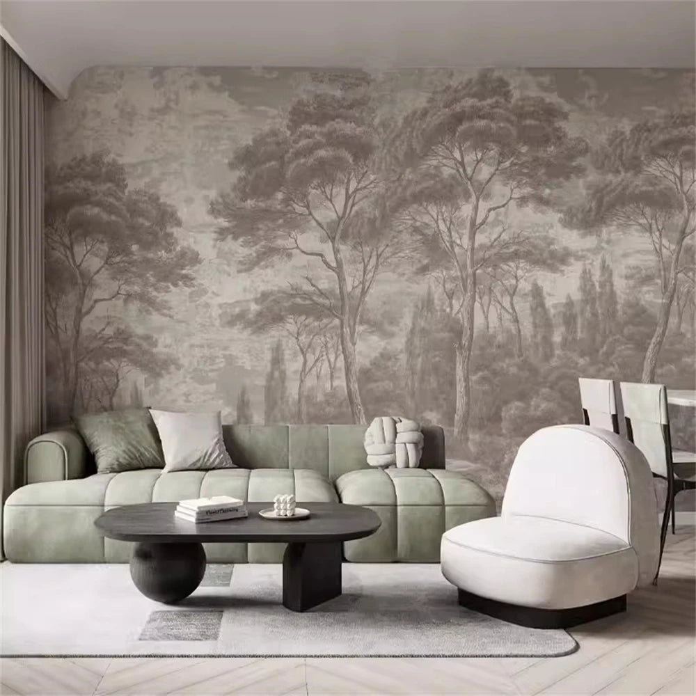 Papier peint panoramique Forêt de pins gravée taupe : forêt de pins gravée en taupe sur un mur patiné, derrière un canapé vert sauge et une chauffeuse blanche