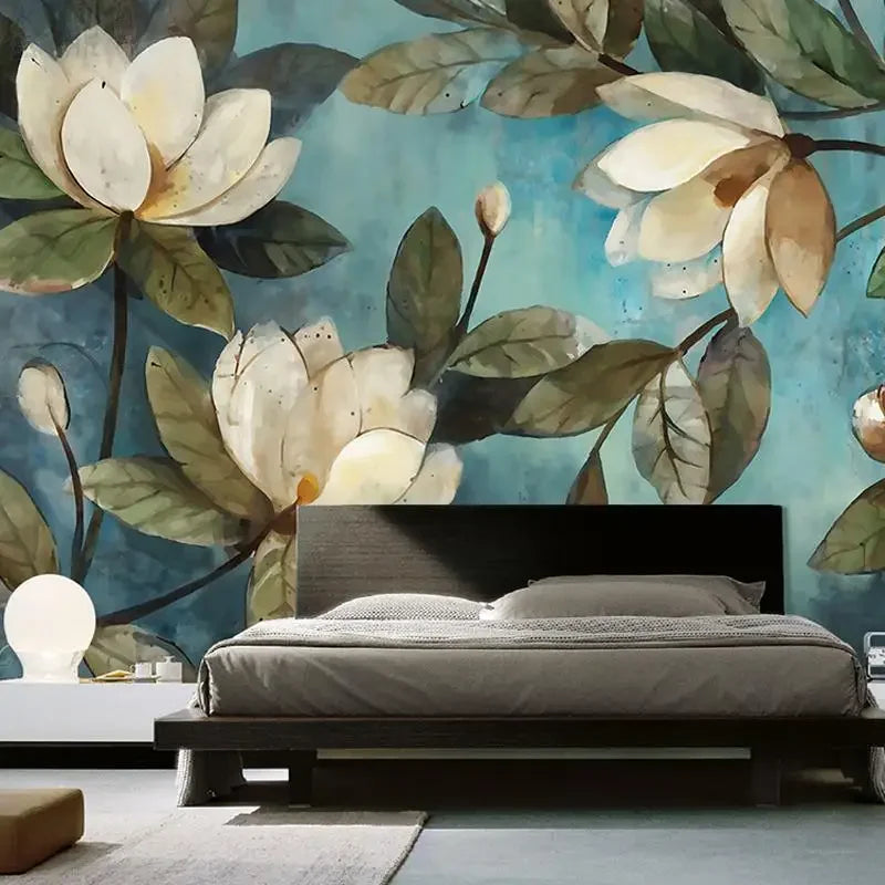 Papier peint panoramique Magnolias peints bleu canard : grandes fleurs de magnolia crème et feuillage olive peints sur fond bleu canard patiné, posé derrière un lit
