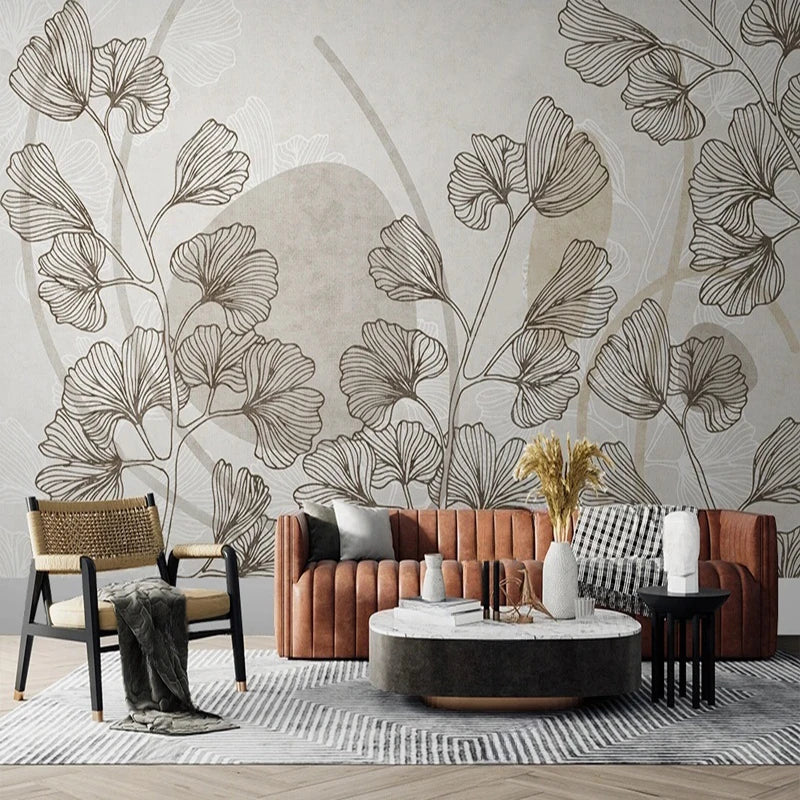 Papier peint panoramique Feuilles de ginkgo et formes sable : branches de ginkgo dessinées au trait sépia sur fond grège, formes rondes sable, derrière un canapé cognac