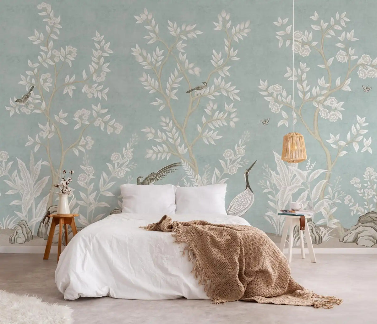Papier peint panoramique Chinoiserie feuillage blanc céladon : chinoiserie au feuillage blanc sur fond céladon derrière un lit blanc, plaid caramel et suspension en rotin