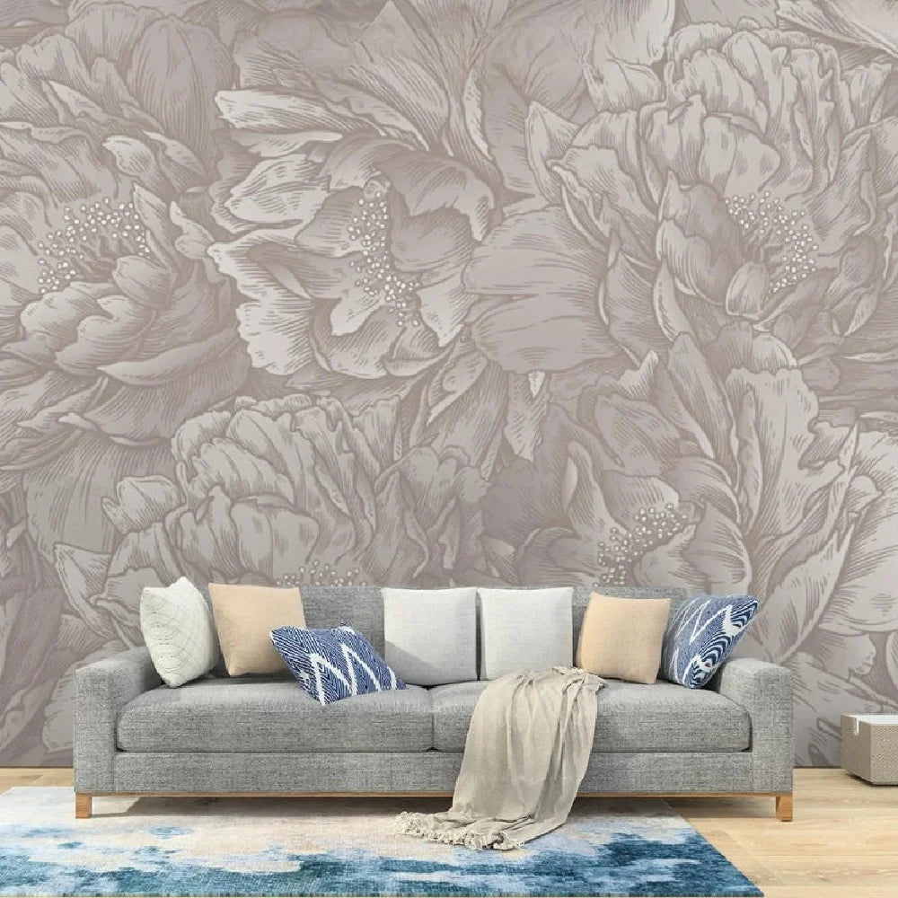 Papier peint effet pivoines gravées taupe : effet pivoines gravées taupe derrière un canapé gris aux coussins beiges et bleus