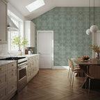 Papier peint effet damas estompé vert sauge : effet damas estompé vert sauge sur le mur d'une cuisine lumineuse, suspensions en verre et table en bois