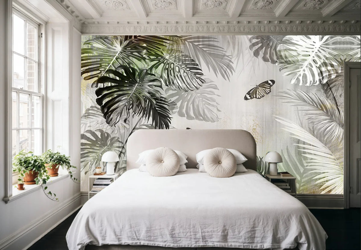 Papier peint panoramique Jungle grisée aux papillons : jungle grisée aux feuilles de monstera et papillons derrière un lit blanc, sous un plafond mouluré