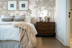 Papier peint panoramique Pins élancés vert sauge sur fond perle posé derrière la tête de lit d’une chambre